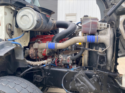 Mack GU533 engine bay view showing turbocharger, hoses, reservoirs, and radiator area with blue hose clamps.