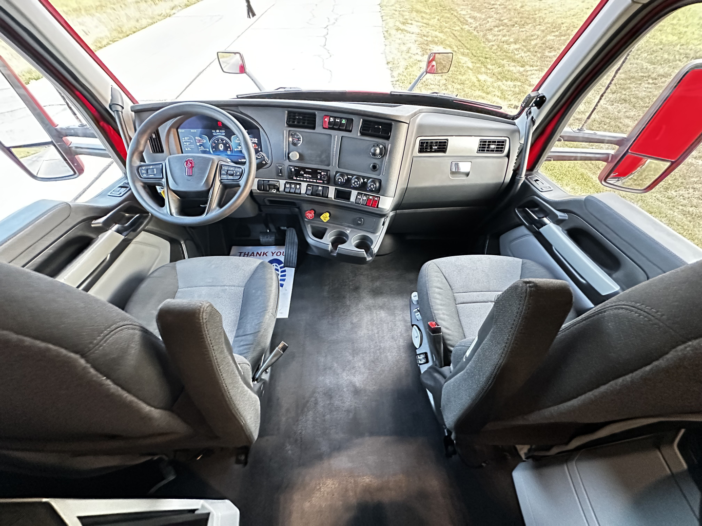 Kenworth T680 cab interior showing steering wheel, dashboard, and front seating from a high angle.