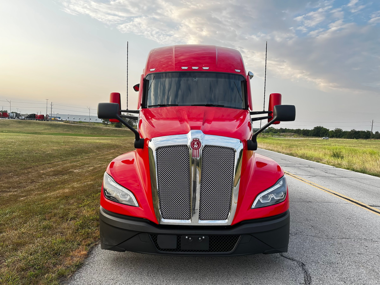 Kenworth T680 truck front view showing bold chrome grille, red cab, black bumper, and side mirrors.