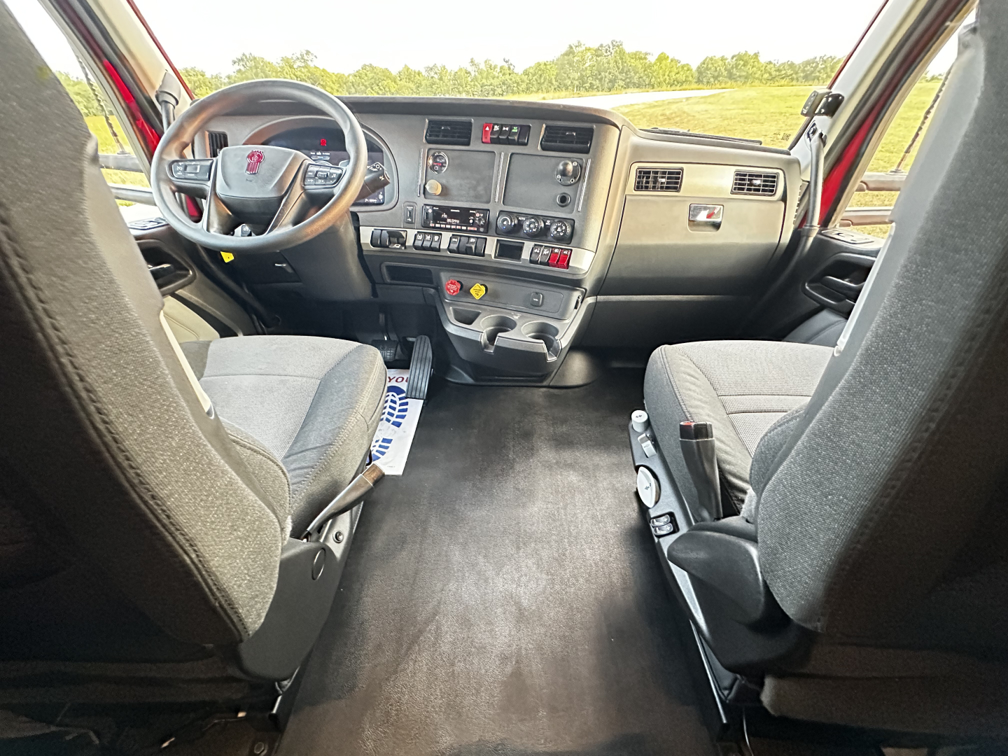 Kenworth T680 interior cab view showing driver and passenger seats and dashboard with steering wheel, center console, and control panels.