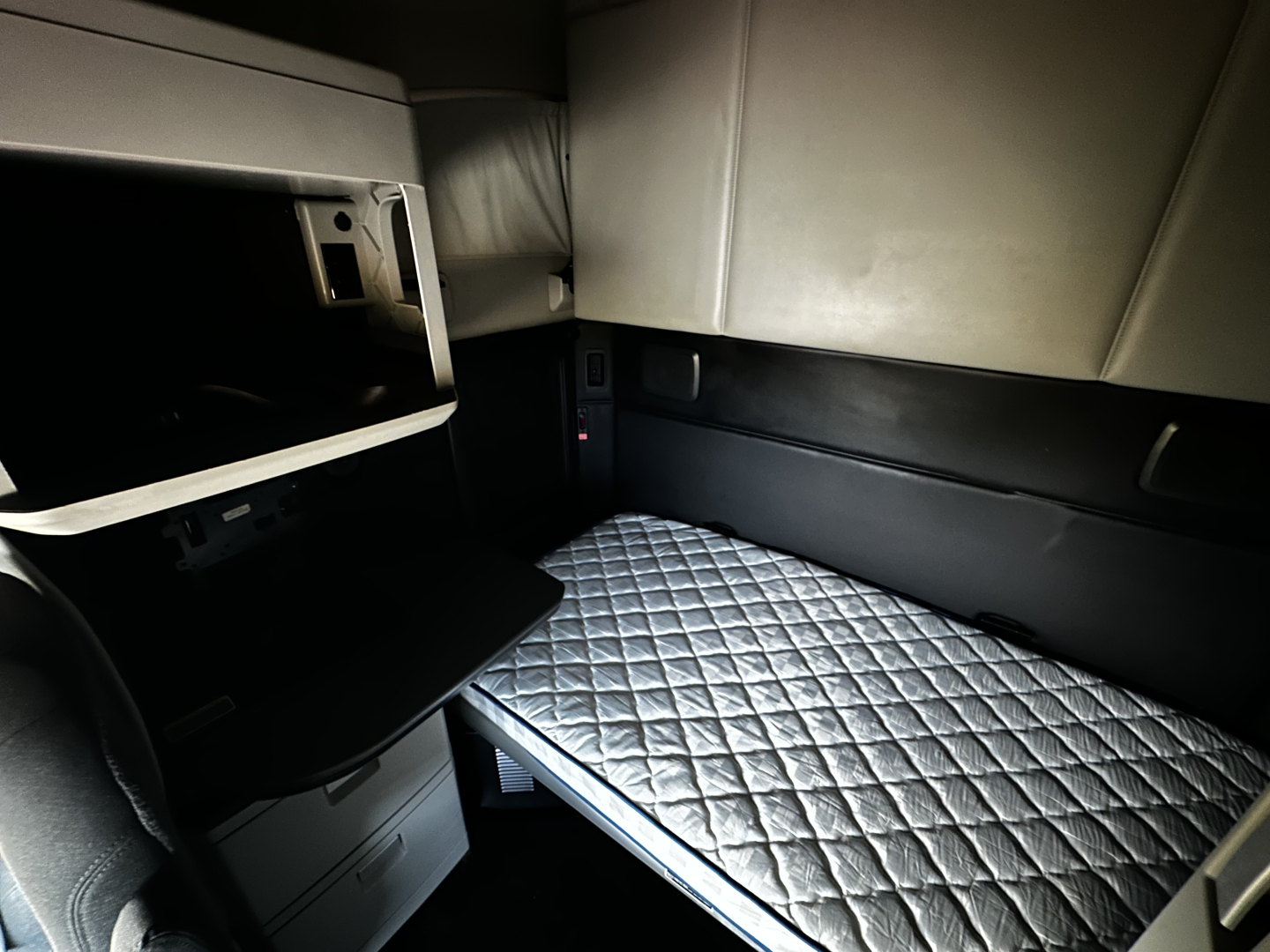 Kenworth T680 sleeper cab interior showing stacked bunk area with quilted mattress, side storage, and dashboard opening