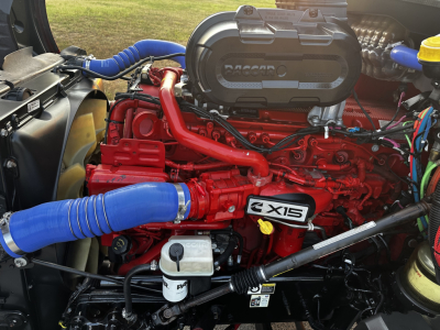 Kenworth T680 engine bay with red 6-CTA engine, blue hoses, and visible air intake cover showing Vol. 2X15 badge; various wiring and reservoirs present.