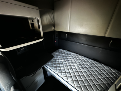 Kenworth T680 sleeper cab interior showing stacked bunk area with quilted mattress, side storage, and dashboard opening