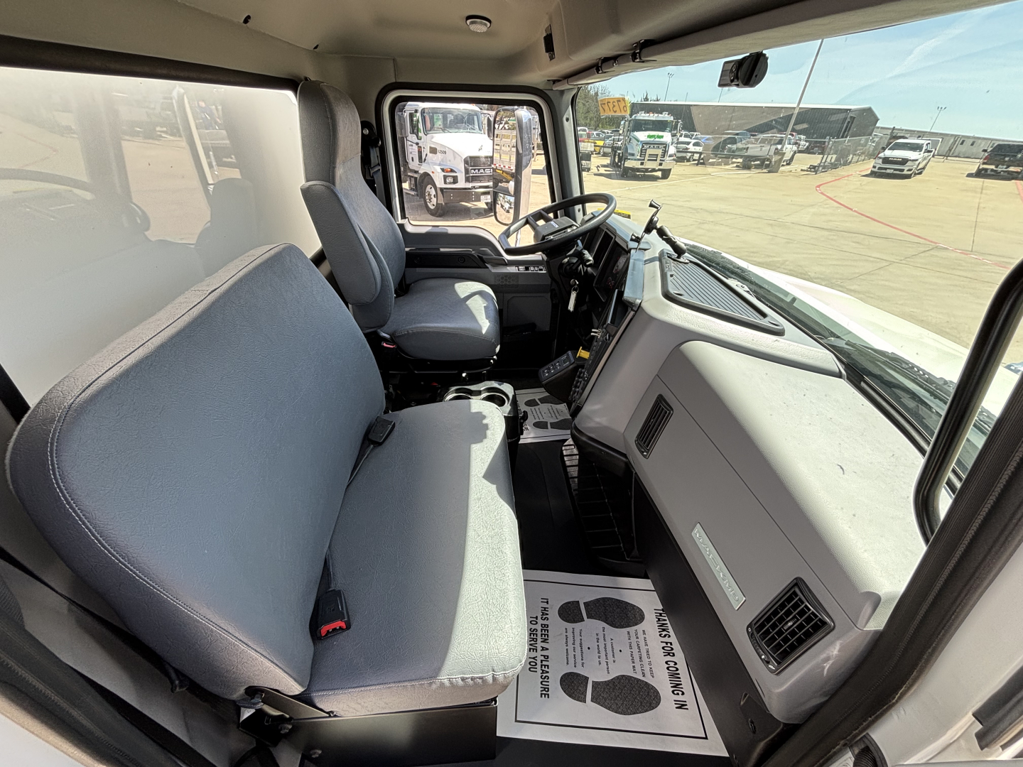 Cab interior of a new 2025 Mack MD7 box truck showing driver seat, passenger seat, steering wheel, and dashboard.