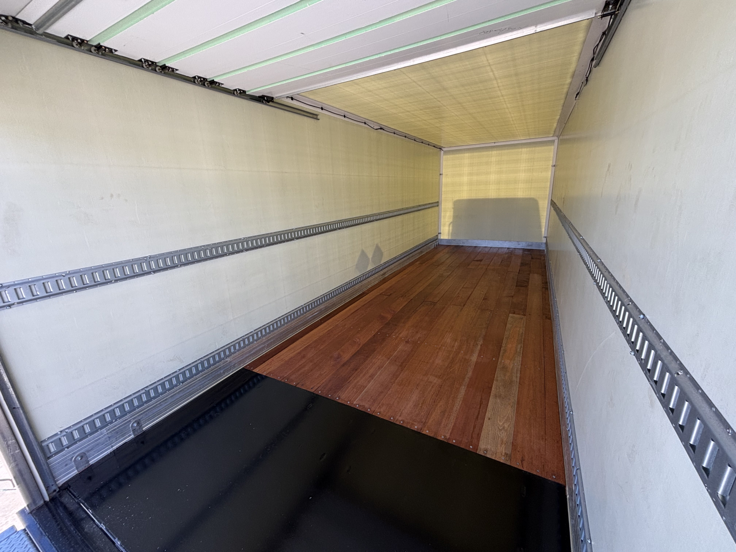 Truck cargo area interior showing empty box trailer with wooden floor and side rails, viewed from doorway.