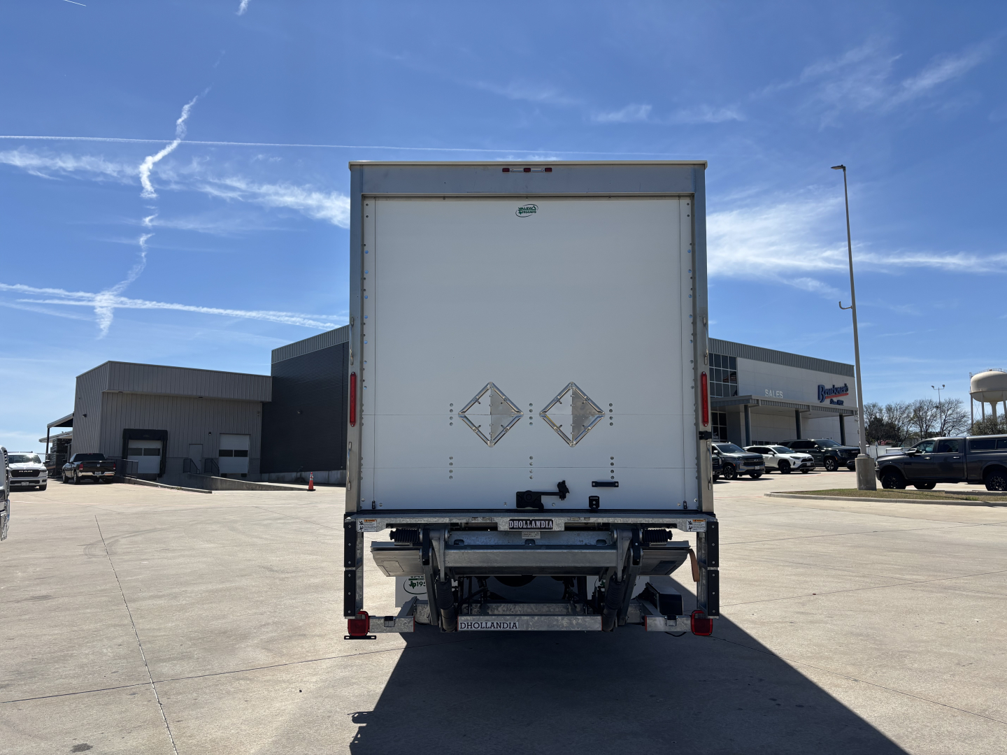 MD7 box truck rear view showing cargo area doors with diamond placards and rear underride guard, tail lights, and bumper.