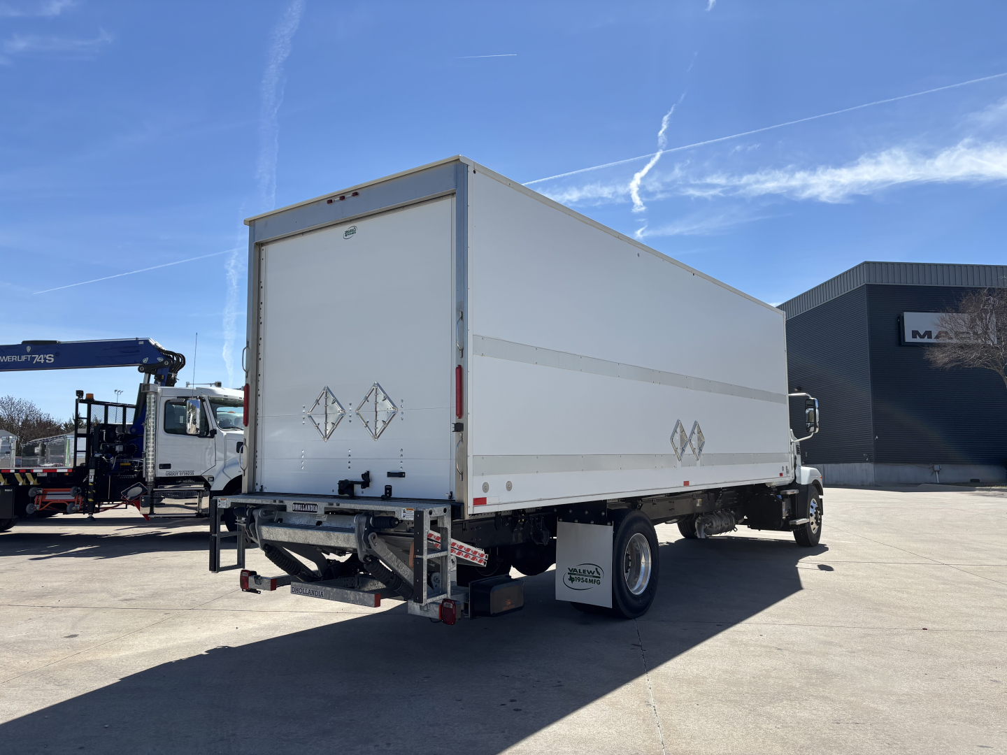 Mack MD7 box truck trailer in a dealership lot showing back doors and side profile with reflective warning diamonds on doors.