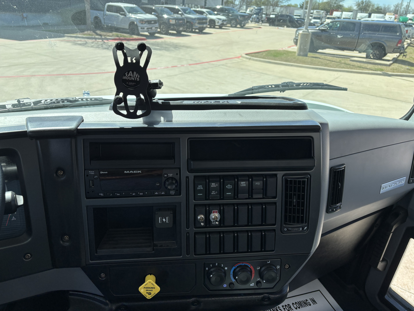 Dashboard view of a 2025 Mack MD7 truck showing steering wheel area, center console, climate controls, radio, and a mobile mount on the dash.