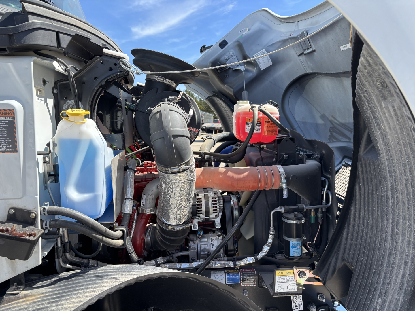 Mack MD7 engine bay showing coolant reservoir, air intake hoses, hoses, and battery area in a new truck.
