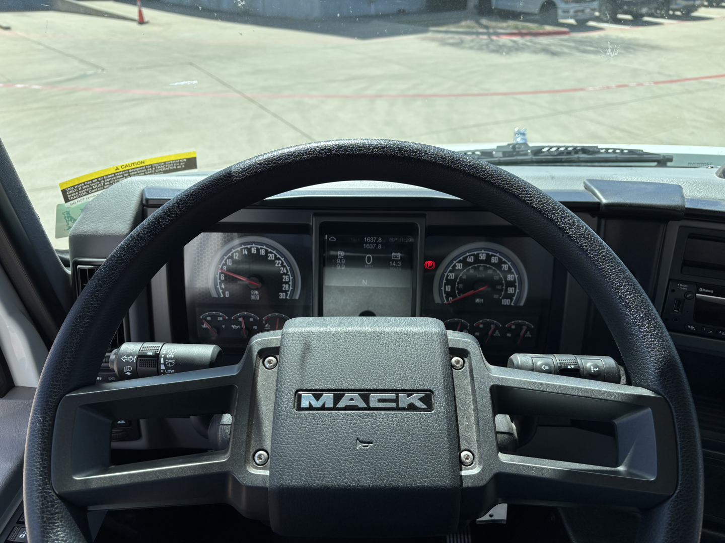 Mack MD7 truck interior steering wheel with dashboard gauges visible through steering wheel, from driver’s seat perspective.