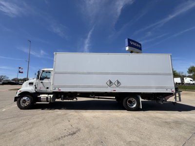Box truck in side profile showing a large rectangular cargo box on a Mack chassis, white exterior, no text legible on side, blue sky. 