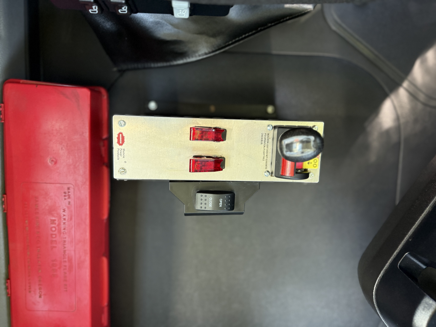 Cab interior showing control panel with red switches, a small digital gauge, and a red safety box; Mack AN64T truck context present