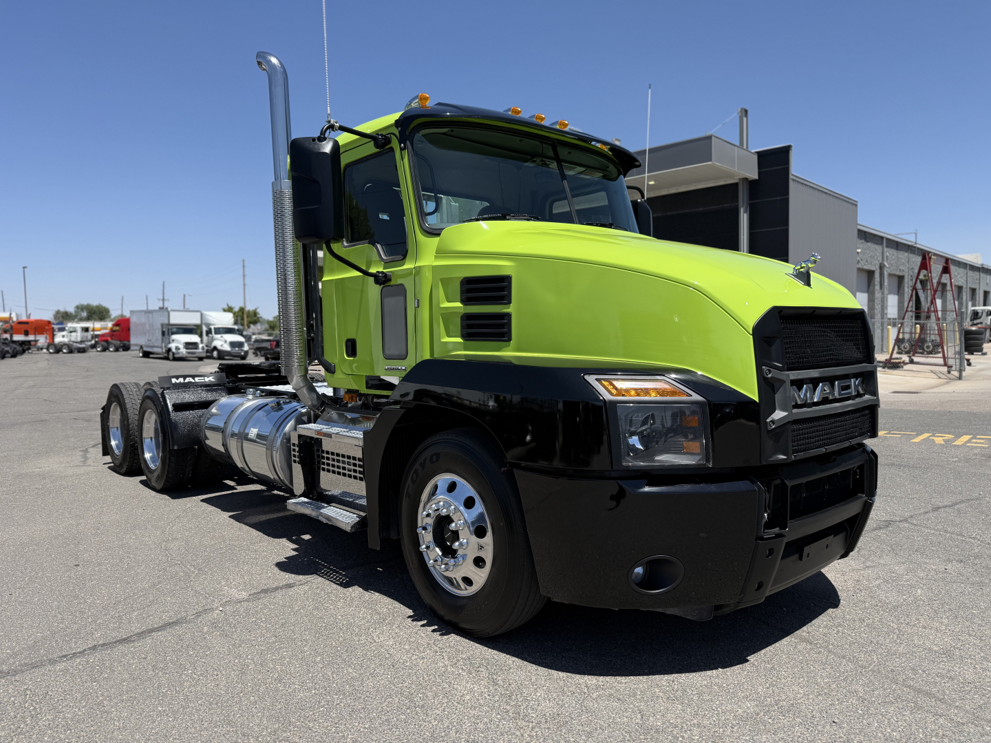 Mack AN64T conventional daycab truck in bright green and black, front three-quarter view, displaying chrome exhaust stack, large grille, and dual rear axles.