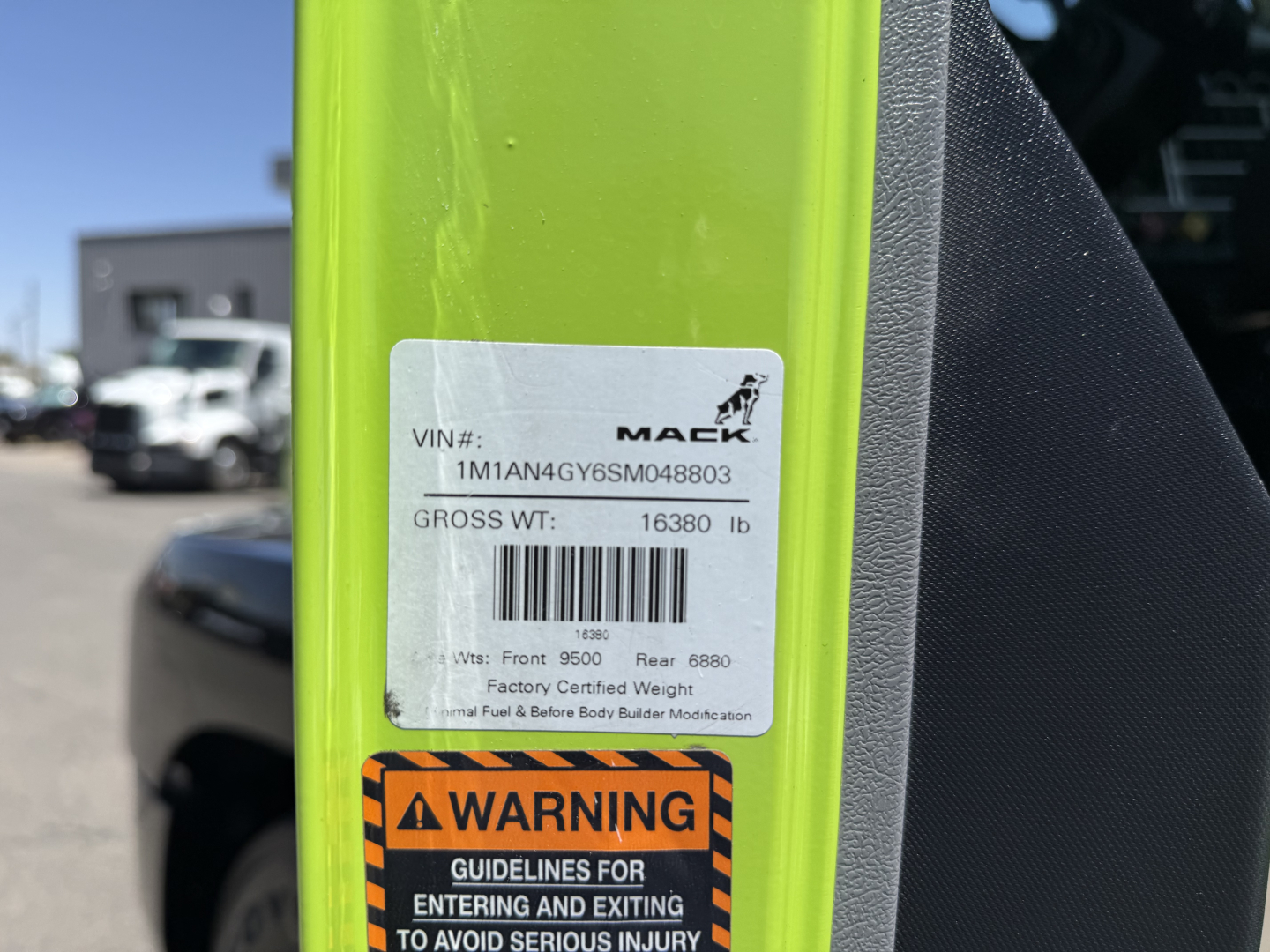Mack AN64T truck VIN label on bright yellow frame showing VIN 1M1AN4GY6SM048803 and gross weight 16380 lb, bar code, and factory weight data plus a warning label.