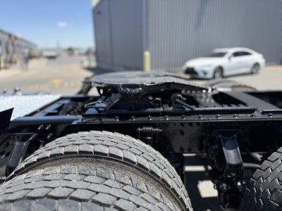 Chassis and dual rear axles of a Mack AN64T truck cabless frame with rear tires in foreground, generic industrial lot in background.