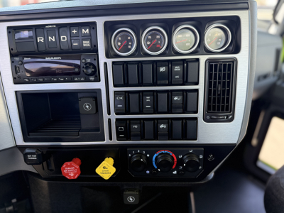 Mack AN64T dash panel showing gauges, switches, and controls in the cab interior. Includes steering area, climate knobs, warning lights, and radio/CD slot.