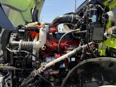 Mack AN64T engine bay showing red Cummins-like diesel engine, black hoses, wiring, and lime green cab interior; various reservoirs and components visible.