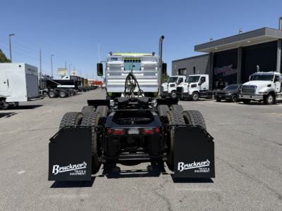 Rear view of a semi truck chassis showing mud flaps with Bruckner's Equipment logos and fifth wheel area, Mack AN64T stock and dealership lot in background.