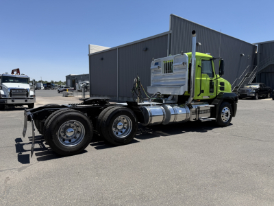 Truck chassis with a bright green Mack AN64T cab in the background. Side view shows a complete tractor with dual rear axles and exposed fuel tanks, no trailer attached.