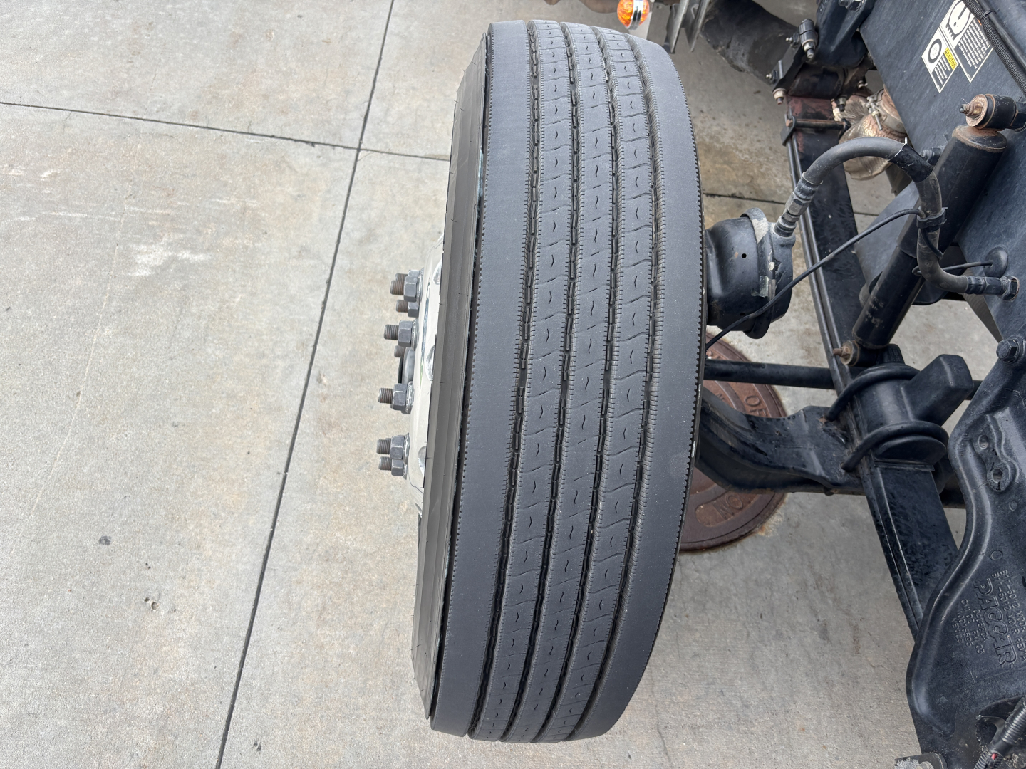 Truck wheel assembly showing front axle with large dual tires, hub studs, and suspension components in a Peterbilt 389 cabover/truck chassis.
