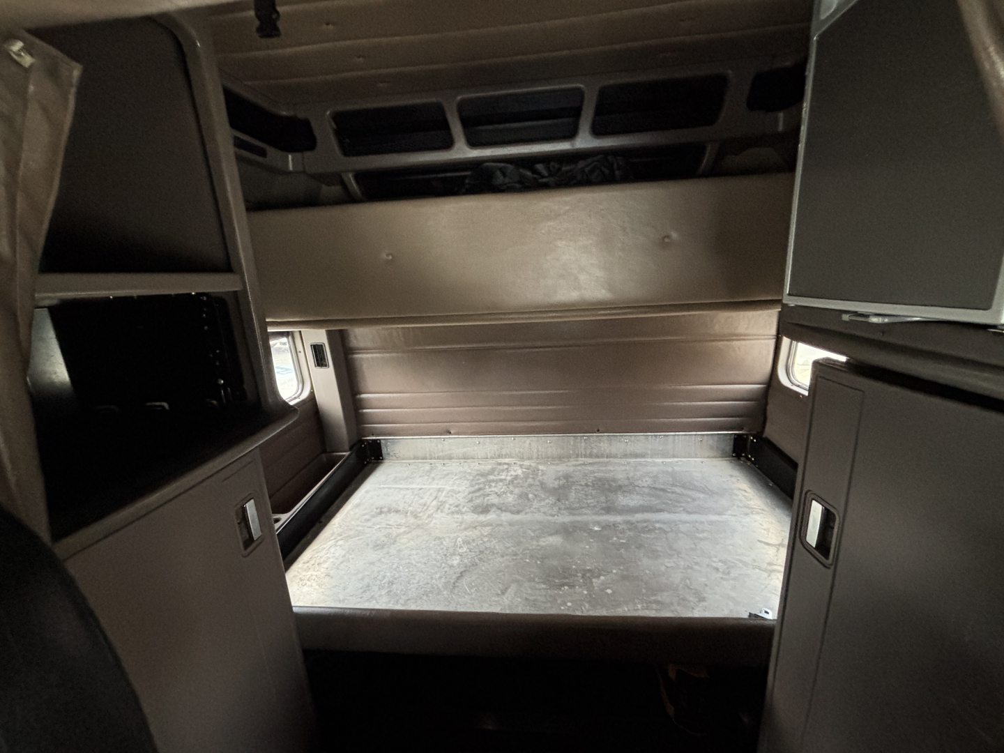 Peterbilt 389 cab interior view showing sleeper area with storage cabinets and bare floor; cabin walls and overhead storage visible.