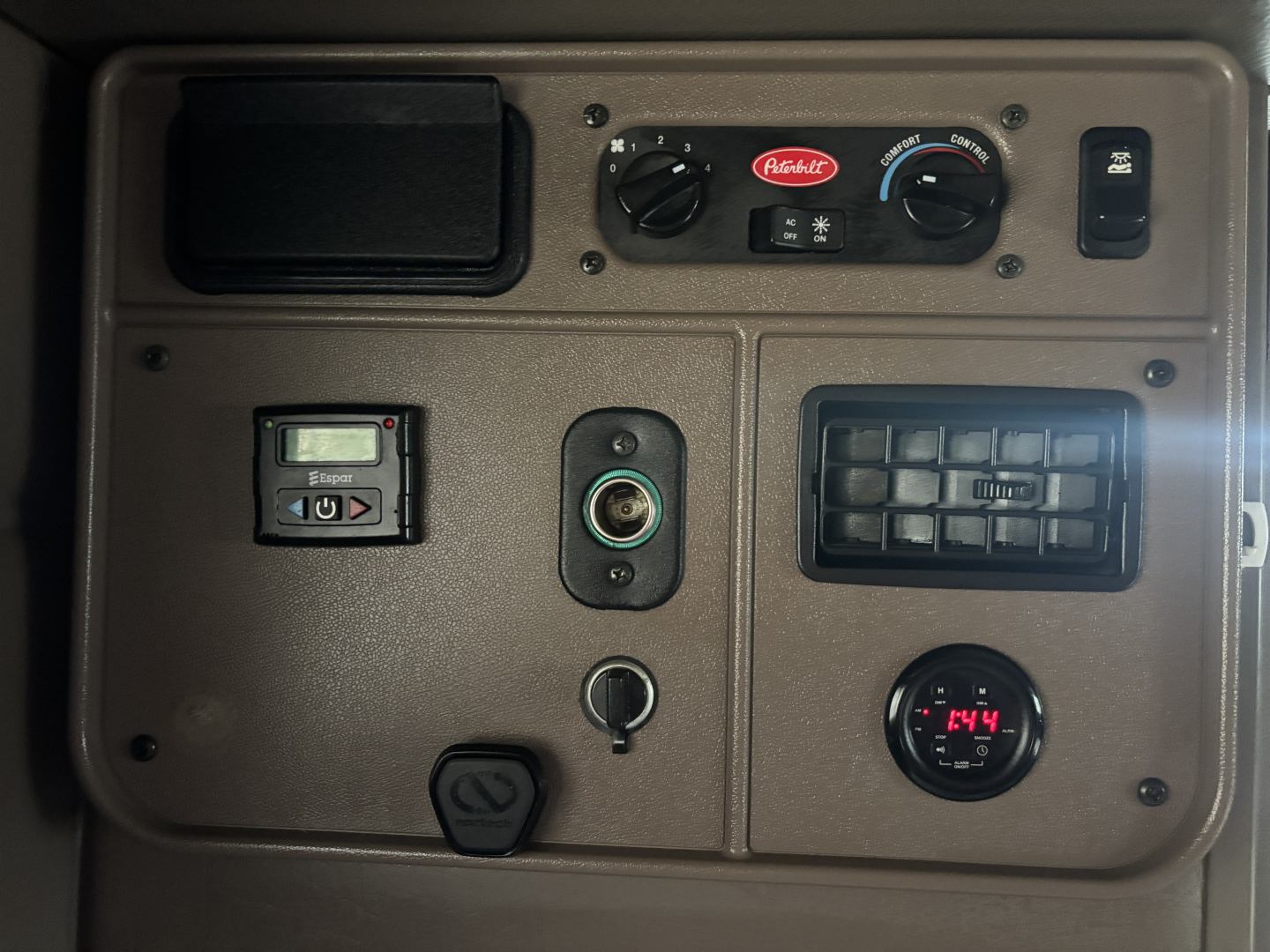 Peterbilt 389 dash panel showing controls and gauges: An Abilene? brand knob, climate controls, electrical outlets, round gauge reading 74, and various sockets.