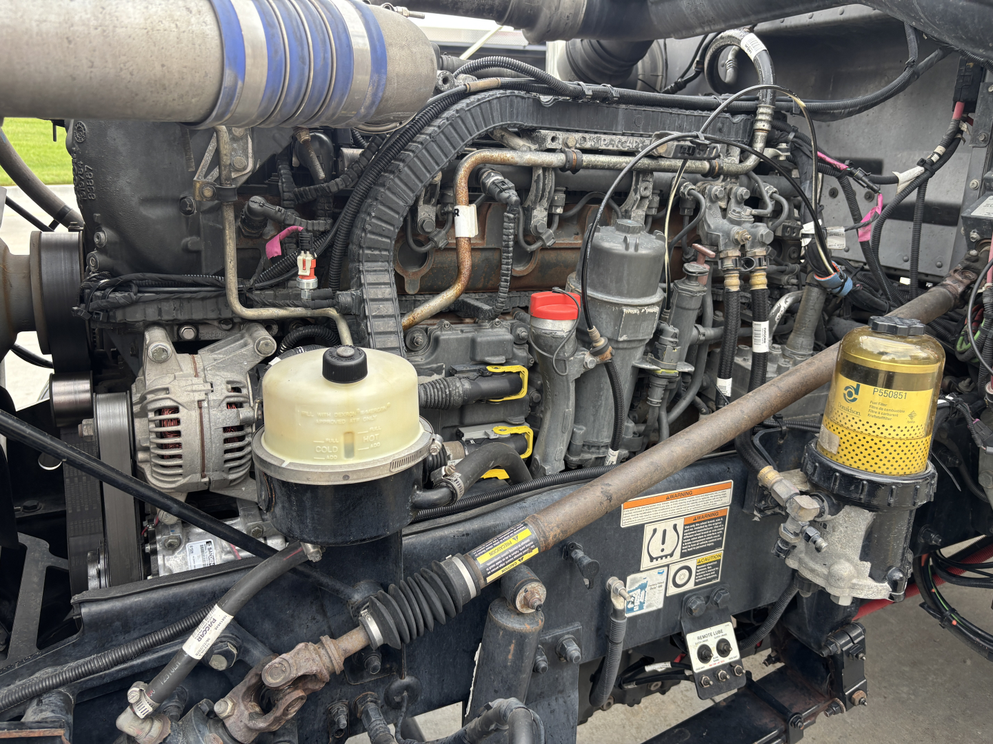 Peterbilt 389 engine bay showing diesel engine components, hoses, reservoirs, and belts.