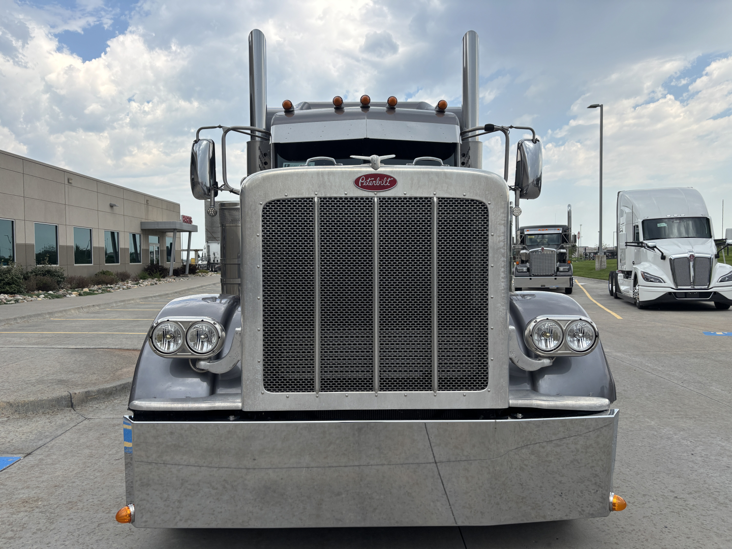 Peterbilt 389 front view showing large grille, dual round headlights, tall exhaust stacks, and chrome bumper with amber marker lights.