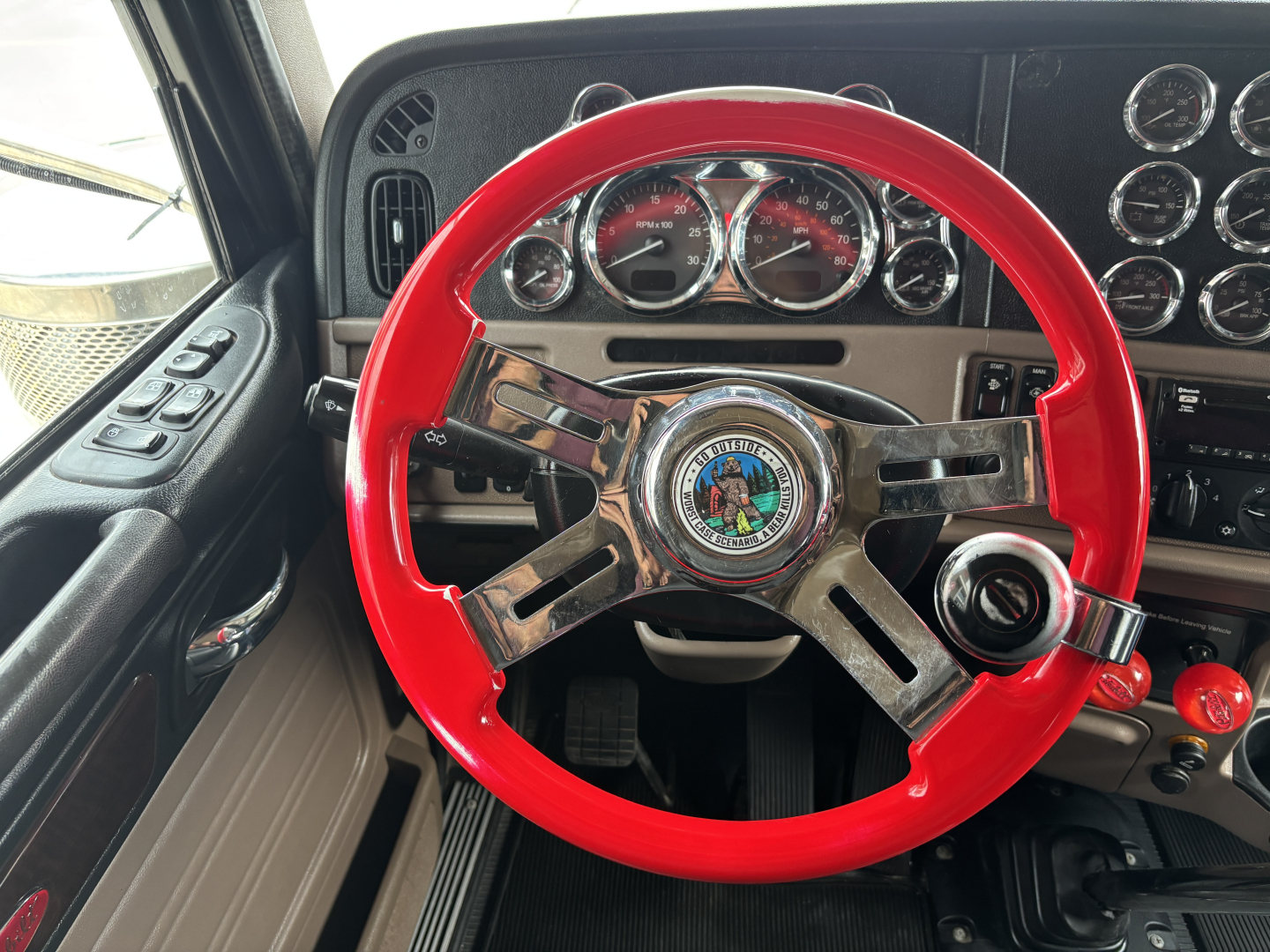 Peterbilt 389 interior steering wheel and dashboard with red steering wheel, gauges, and controls visible.