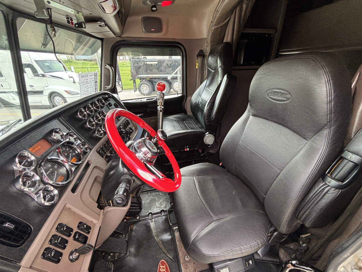 Peterbilt truck interior showing red steering wheel, dashboard with multiple gauges, gear shifter, and black leather seats.