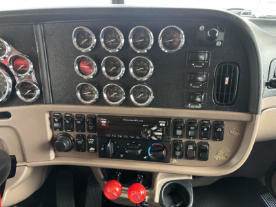 Dashboard of a Peterbilt truck showing multiple round gauges, control switches, radio, climate controls, and two red knobs in the lower console.