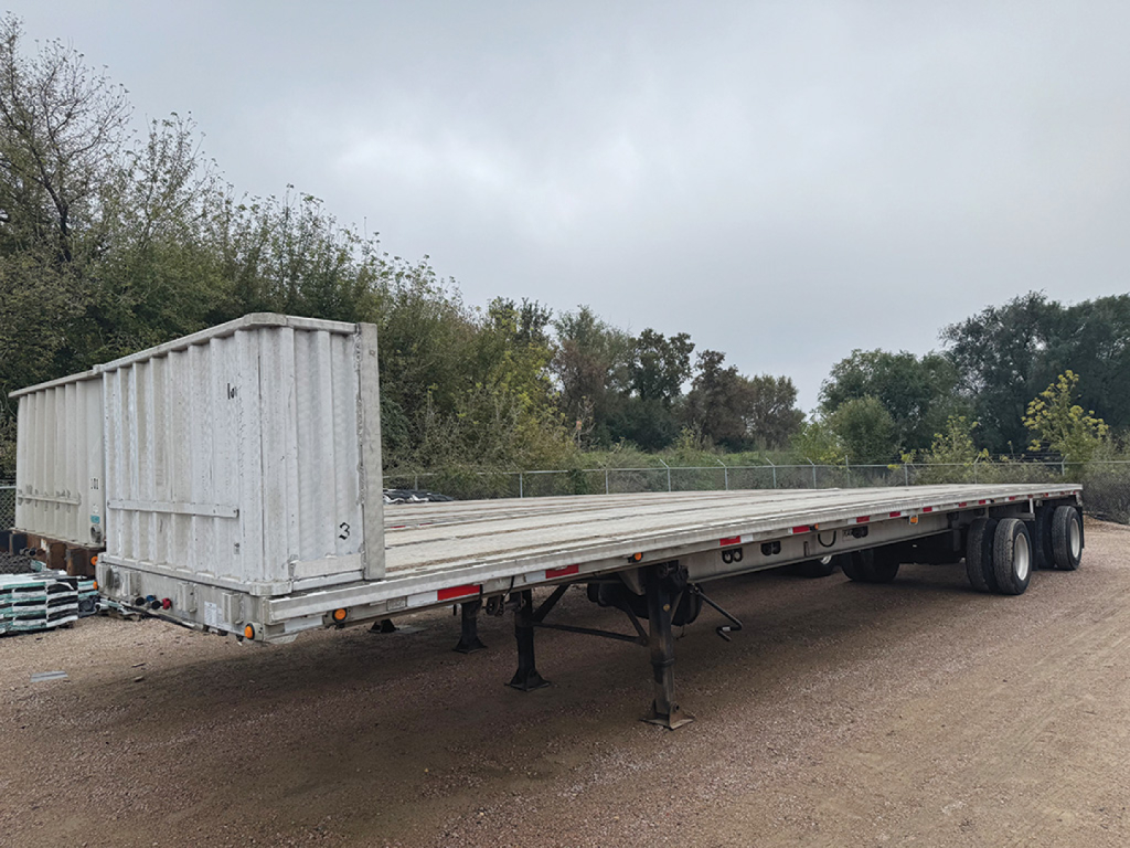Ravens aluminum flatbed trailer showing long flat deck with gooseneck rear, tandem axles, and drop legs in a yard.