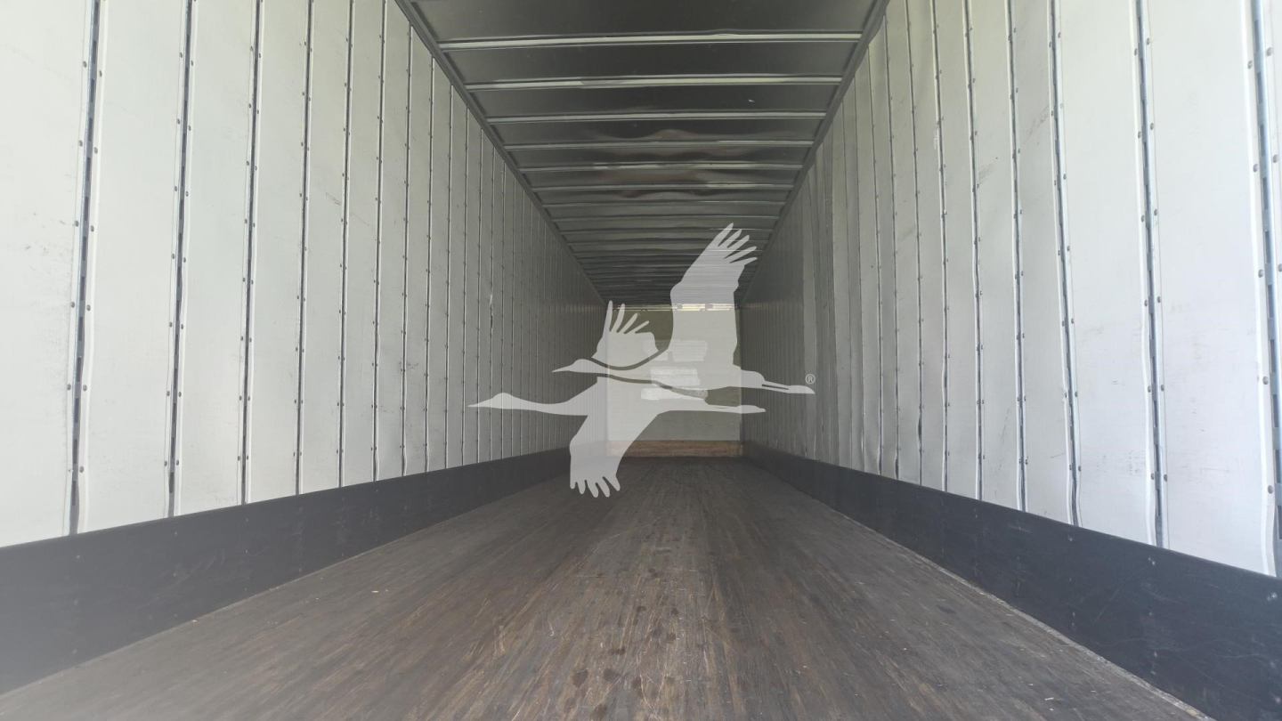 Trailer interior looking down a long cargo area with wooden floor and metal side walls; a watermark of birds is overlaid.