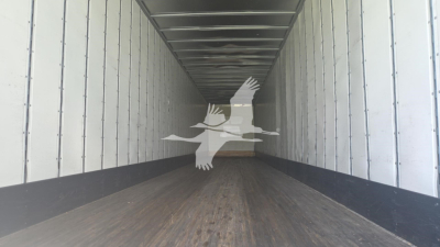 Trailer interior looking down a long cargo area with wooden floor and metal side walls; a watermark of birds is overlaid.