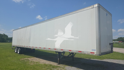 Trailer side with white graphic of birds in flight. Long silver trailer with dual rear wheels on a level field under a blue sky.