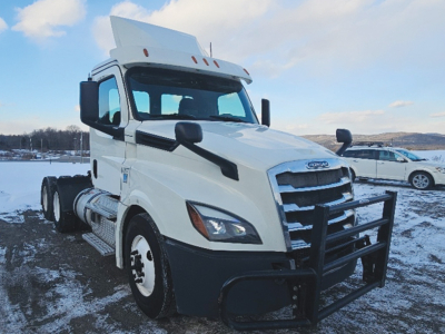 Front left view of a white Freightliner Cascadia126 daycab truck showing grille guard and dual exhaust with snow background.