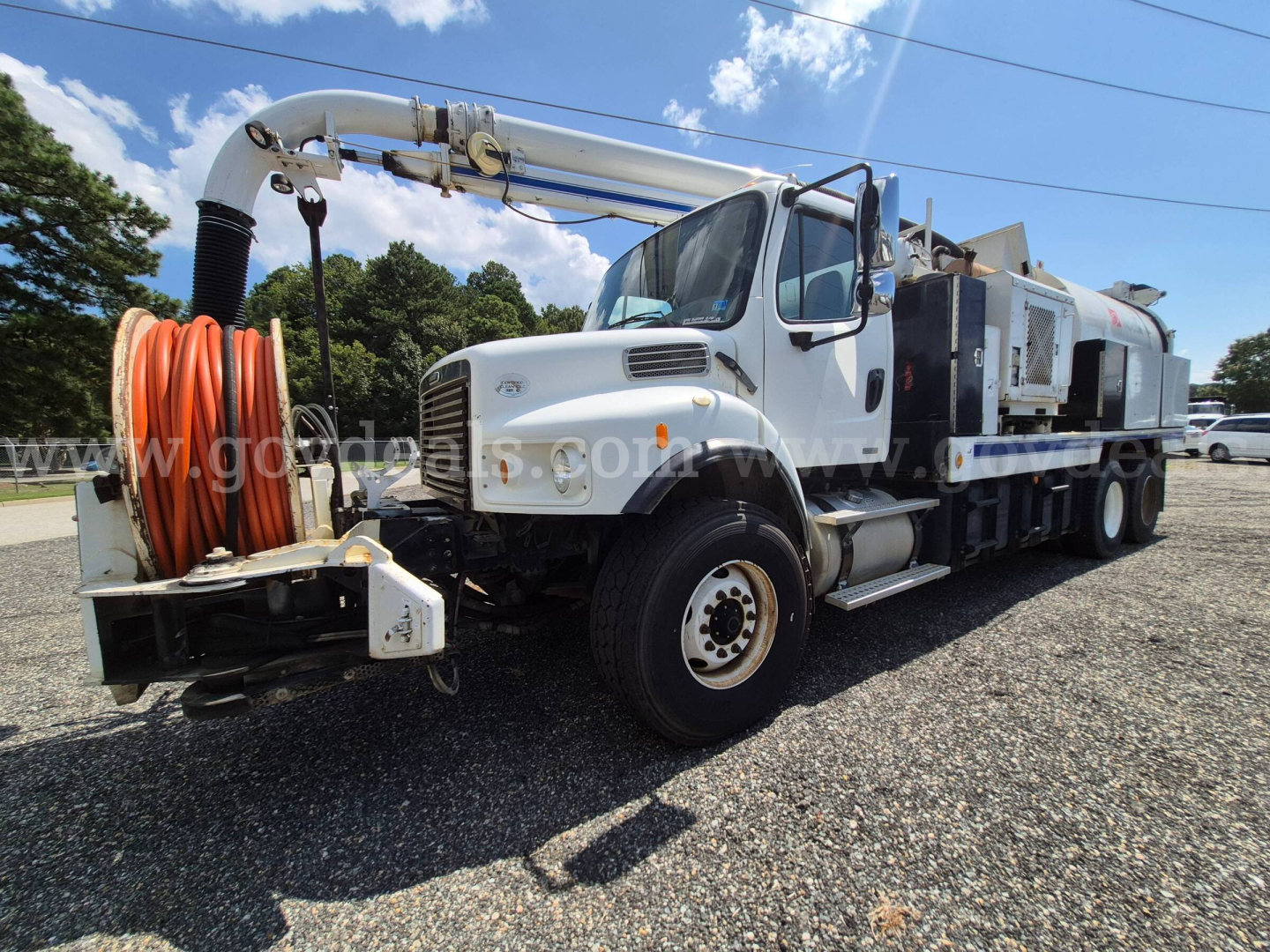Freightliner M2 106V vacuum truck with large orange hose reel on front bumper and long hose reel on a white cab chassis