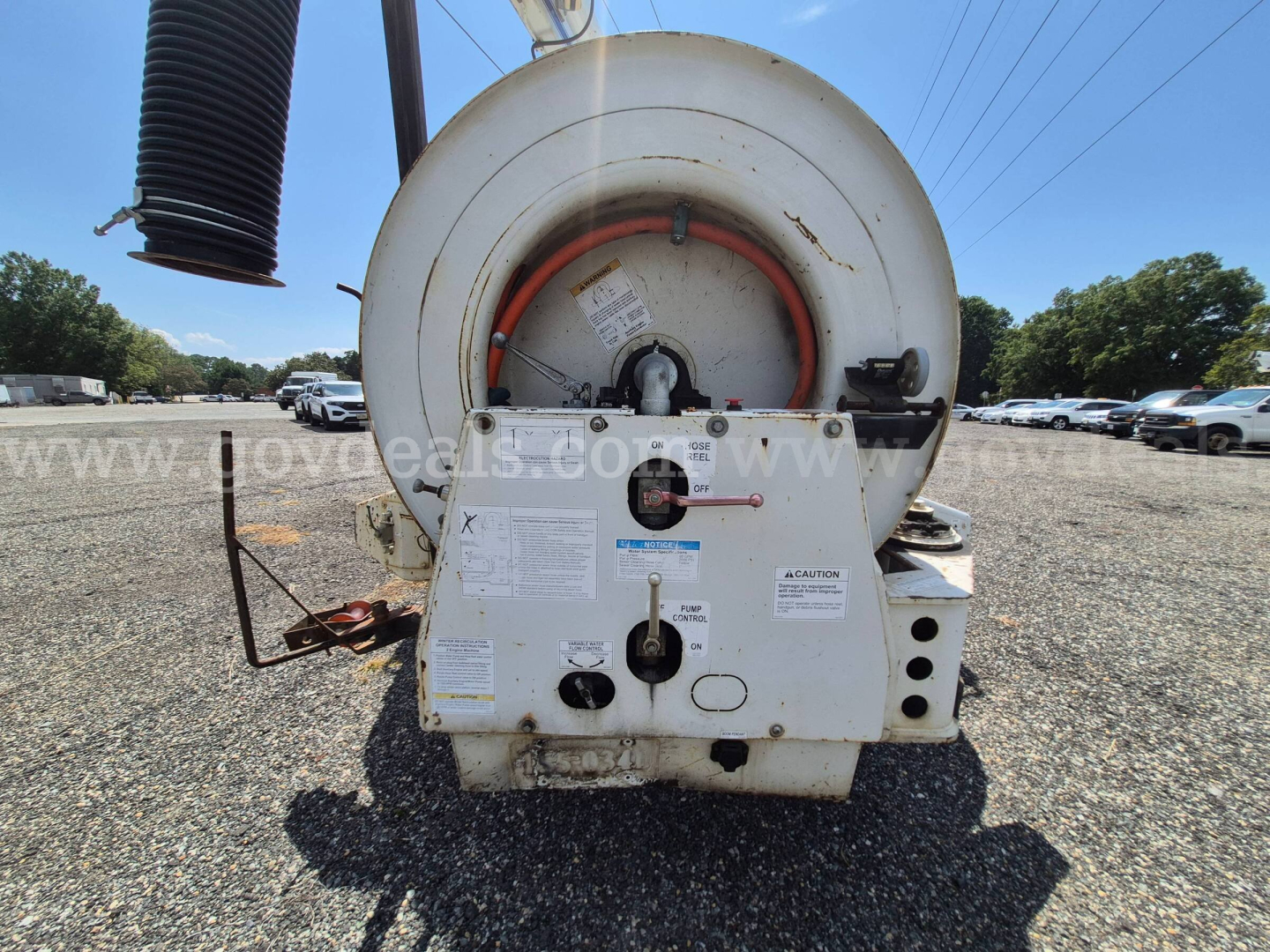 Back of a Freightliner vacuum truck showing circular hose reel and control panels with labels and warning stickers.