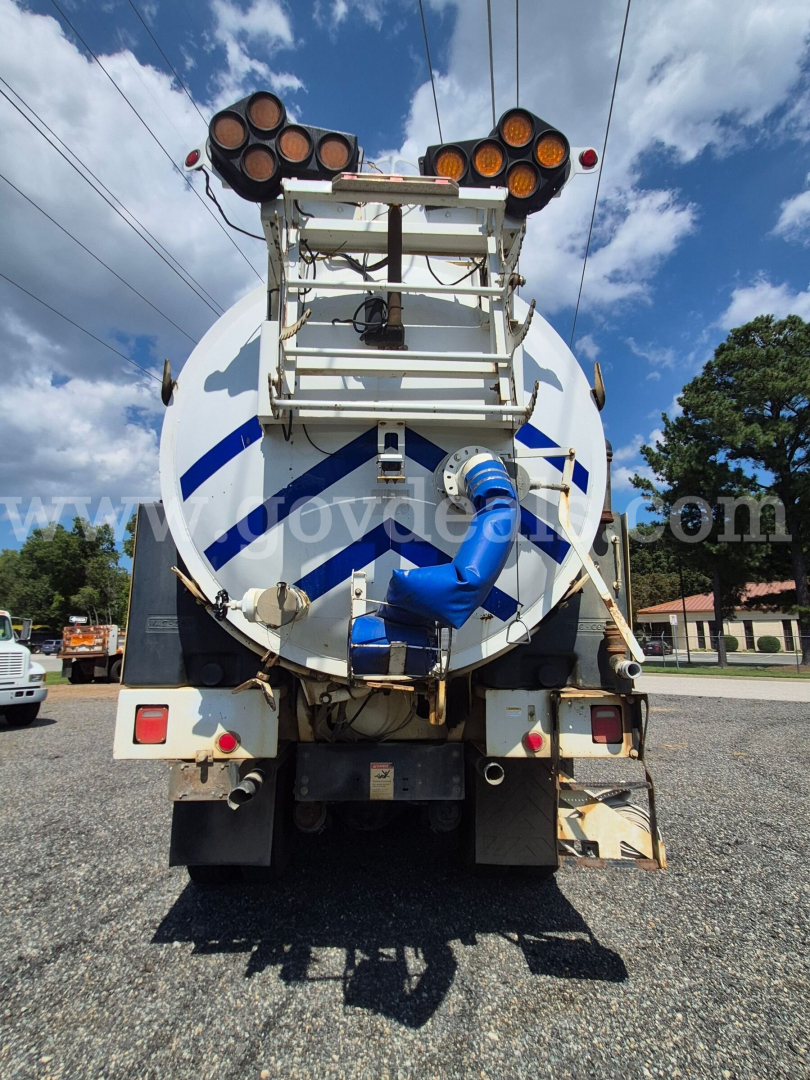 Back view of a 2011 Freightliner M2 106V vacuum truck showing rear-mounted circular tank with blue stripes, ladder, piping, and multiple round light clusters on top.