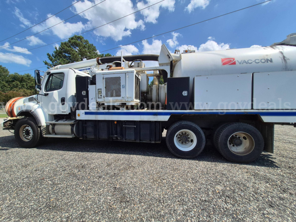 Freightliner M2 vacuum truck side view showing VAC-CON tank and equipment compartment with ladder and hoses.