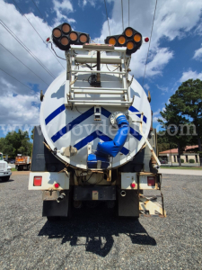 Back view of a 2011 Freightliner M2 106V vacuum truck showing rear-mounted circular tank with blue stripes, ladder, piping, and multiple round light clusters on top.