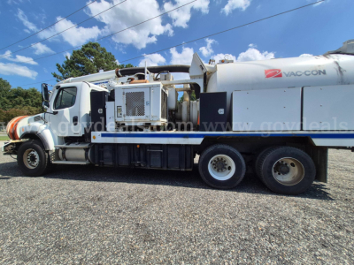 Freightliner M2 vacuum truck side view showing VAC-CON tank and equipment compartment with ladder and hoses.