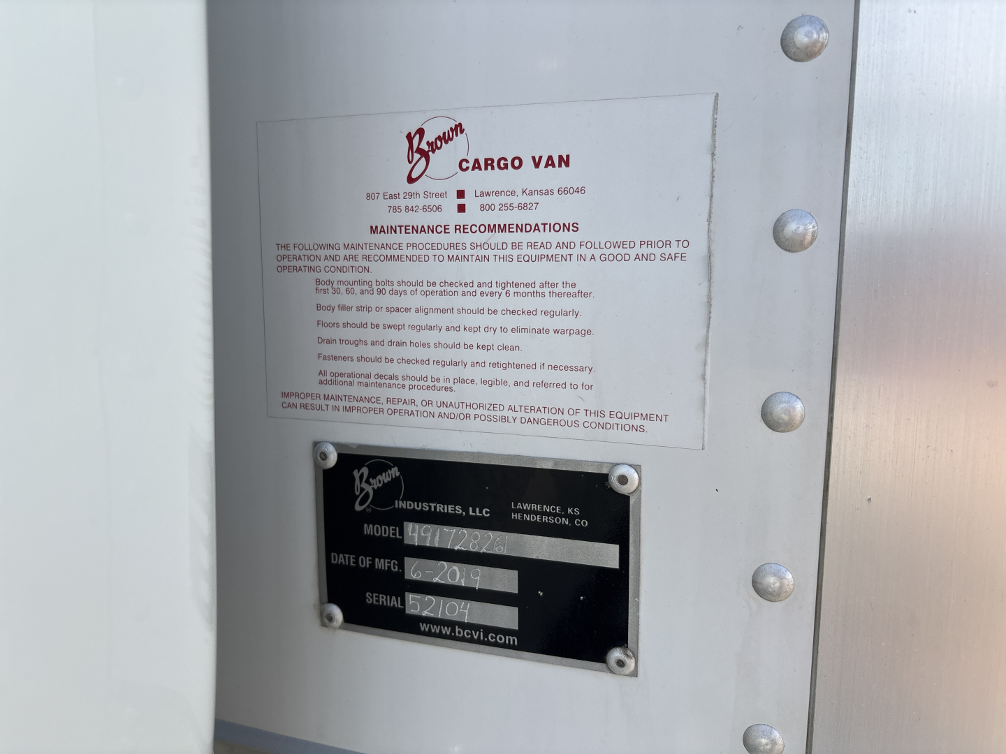 Metal door with maintenance label and serial plate mounted; shows 'Boon Cargo Van' label and a black plate with model, date of mfg, and serial information.