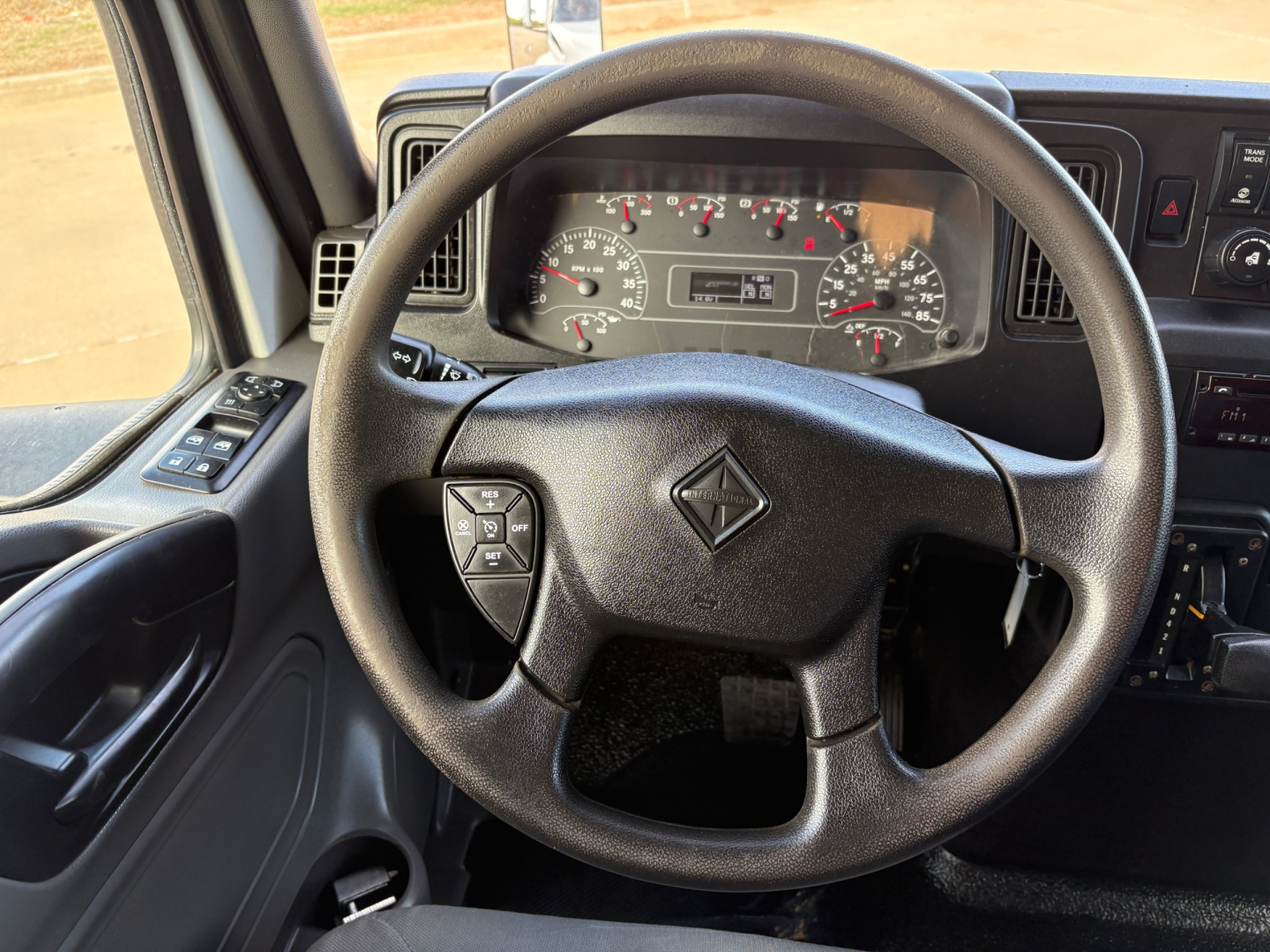 Truck cab interior showing steering wheel and dashboard gauges from International MV607 with steering wheel center diamond logo and instrument cluster.