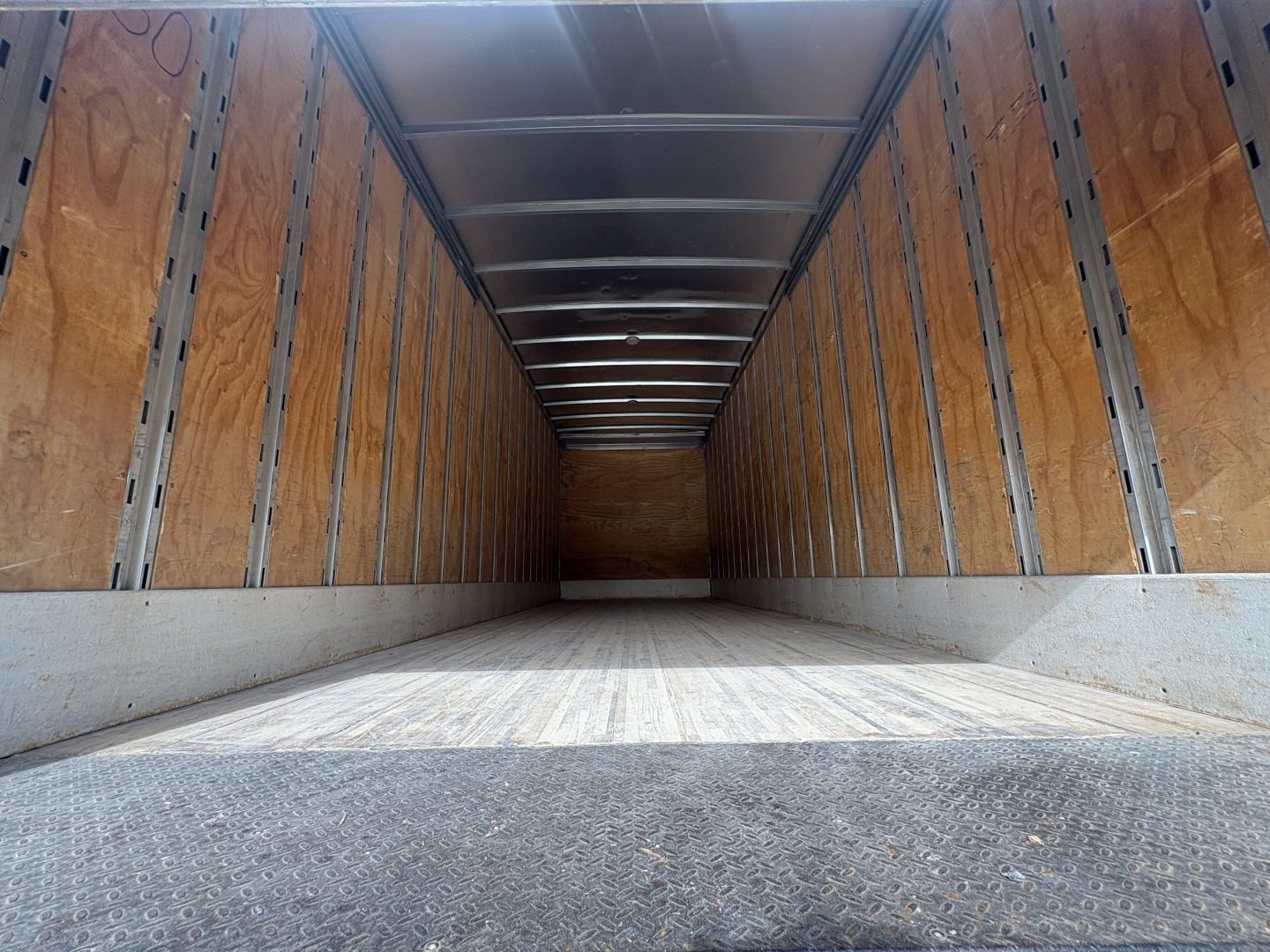 Truck trailer empty cargo area with wooden side walls and metal rails, interior seen from back doorway, long rectangular box truck trailer