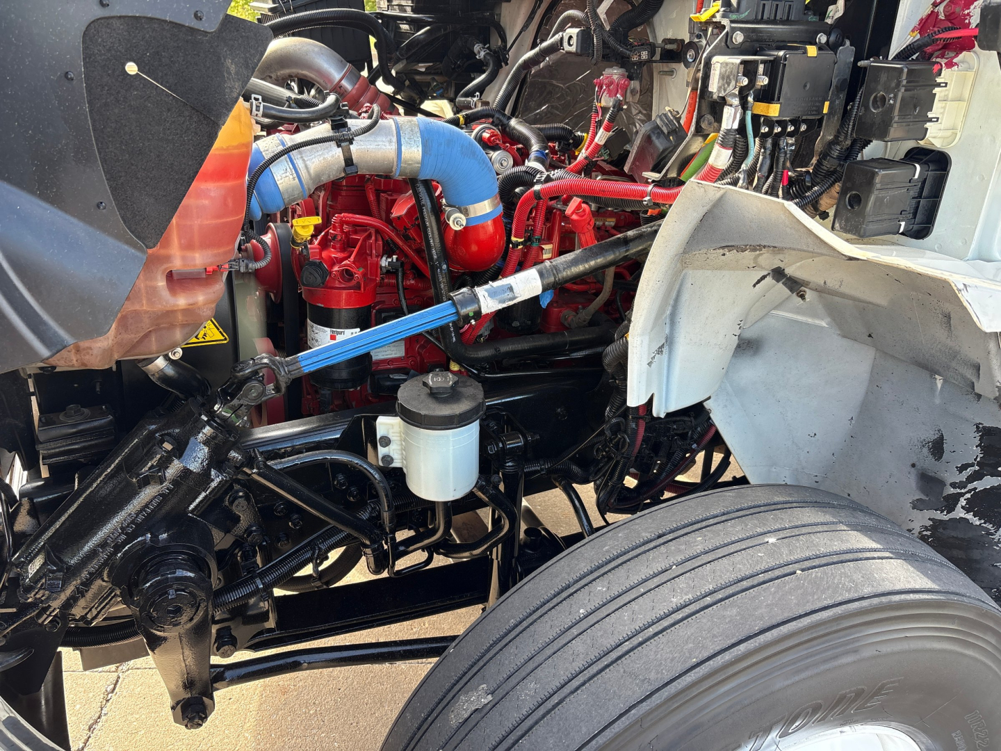 Truck engine bay with blue intercooler hose, red engine components, coolant reservoir, and suspension visible in a 2020 International MV607.