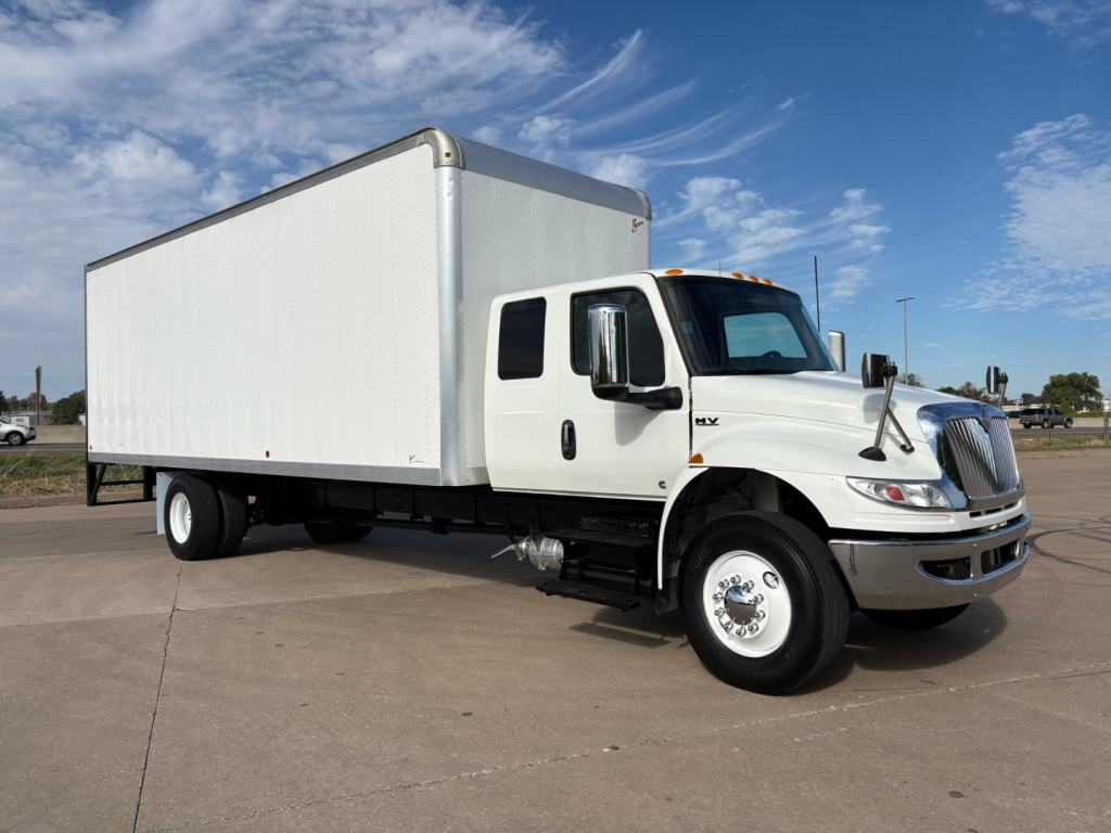 Side view of a white 2020 International MV607 box truck with a large cargo box, black chassis, and dual rear wheels under a clear sky.