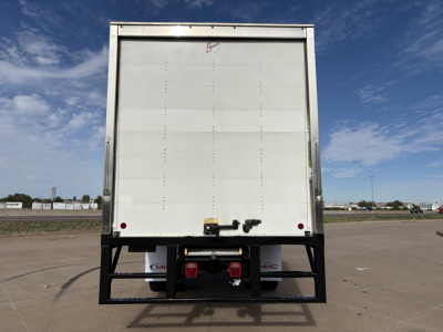 Box truck rear showing cargo area with a metal roll-up door and bumper with red taillights and hitch.