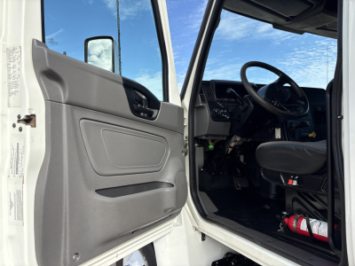 Truck cab interior with open driver door showing steering wheel, dashboard, and seat. Visible text on door panel and controls.