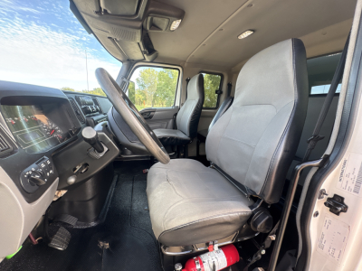 Cab interior of a used 2020 International MV607 truck showing grey fabric seats, steering wheel, dashboard, pedals, and doorway interior.
